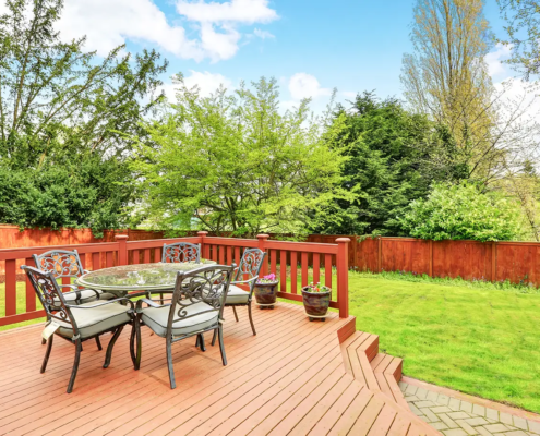 Custom-built wooden deck with a dining area and lounge chairs, enhancing a backyard’s aesthetic and functionality.