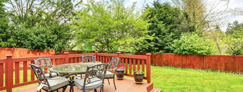 Custom-built wooden deck with a dining area and lounge chairs, enhancing a backyard’s aesthetic and functionality.