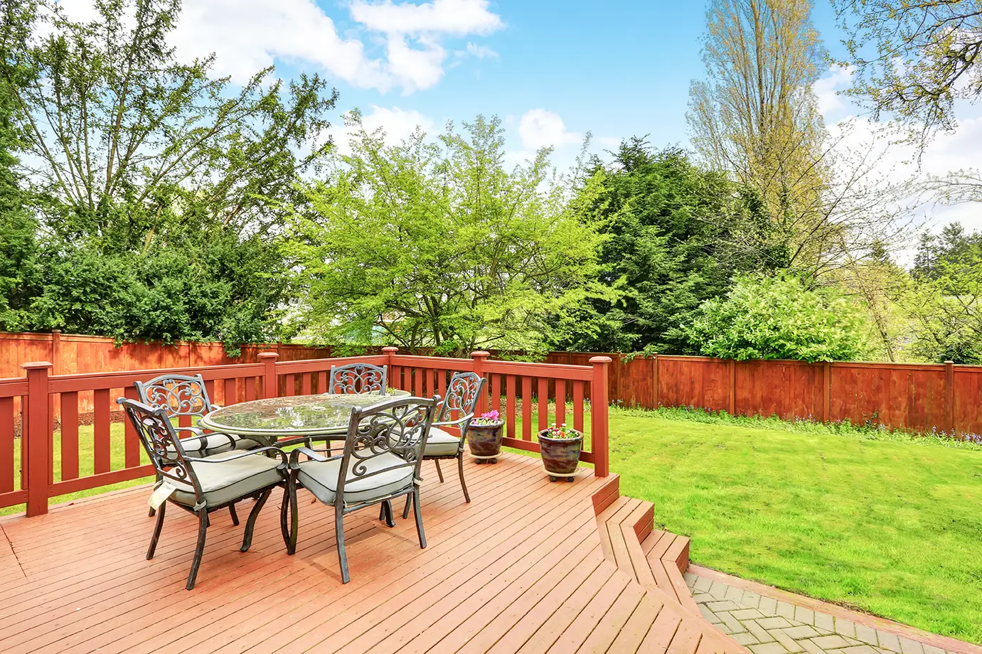 Custom-built wooden deck with a dining area and lounge chairs, enhancing a backyard’s aesthetic and functionality.